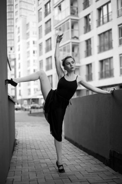 Tutu balerin zarif bir poz yapar. Siyah elbise li ve şehir arka planı üzerinde dans eden güzel genç bir kadın. Açık havada dans yapan muhteşem bir balerin portresi. Siyah beyaz