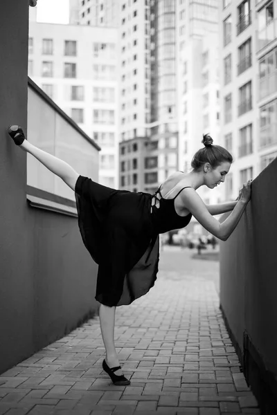 チュチュのバレリーナはエレガントなポーズをとります。黒いドレスとポイントダンスの美しい若い女性は、都市の背景の上に踊ります。屋外でダンスを披露する豪華なバレリーナの肖像画。白黒 — ストック写真