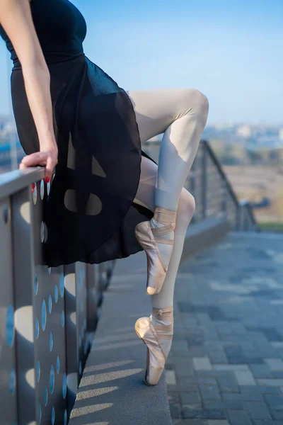 Baletnica w baletkach w buty i czarny taniec Tutu przez ogrodzenie. Piękna młoda kobieta w czarnej sukni i Pointe taniec na zewnątrz. Wspaniała baletnica wykonujący taniec na świeżym powietrzu. Zbliżenie — Zdjęcie stockowe