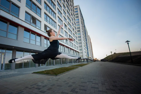 Balerina Tutu pózol ellen lakóépület. Gyönyörű fiatal nő, fekete ruhában és Pointe cipő jumping hihetetlen rugalmasságot. Balerina végez elegáns jumping alakváltozás. — Stock Fotó