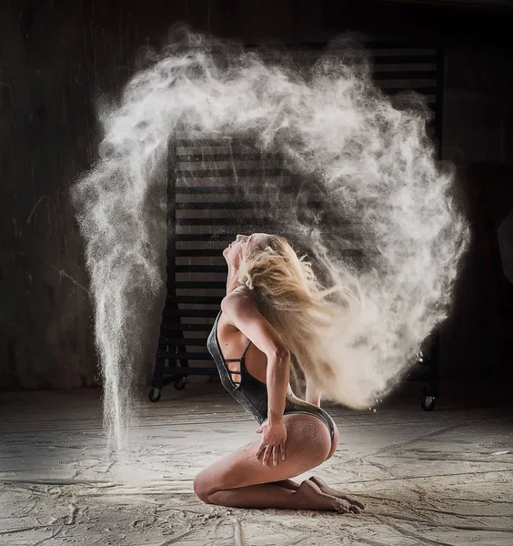 Beautiful blonde dancing in clouds of flour. Woman throws flour into the air.