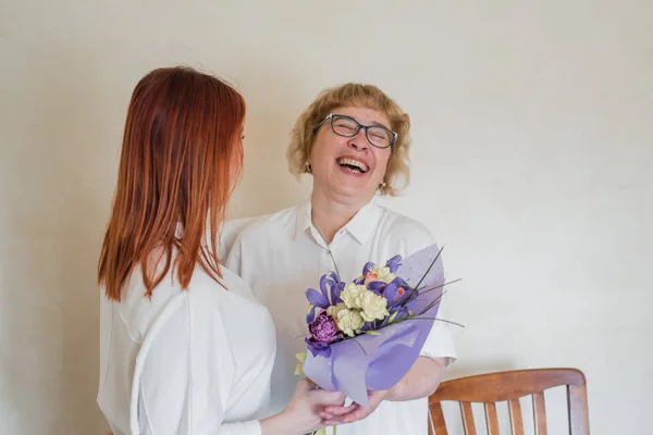 Daughter giving flowers to adult mother. Daughter gives flowers to her mother and hugs her. Spending time together, celebrating at home on weekends. Mothers Day