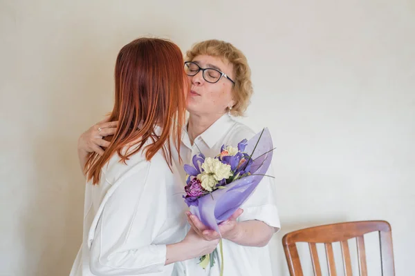 Daughter giving flowers to adult mother. Daughter gives flowers to her mother and hugs her. Spending time together, celebrating at home on weekends. Mothers Day