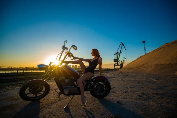 Mujer pelirroja en lencería sexy en tacones altos se sienta en una motocicleta. Atractiva chica pelirroja se sienta en una motocicleta al atardecer — Foto de Stock