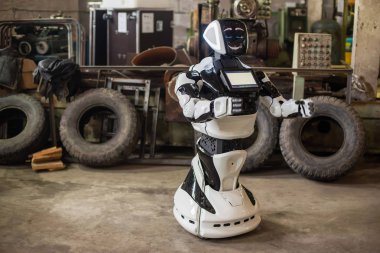 Ellerini göğsüne, bir ekran ile gezici, insansı, beyaz bir robot taşır. Bu eski makineleri ile kirli, darmadağın bir garajda duruyor