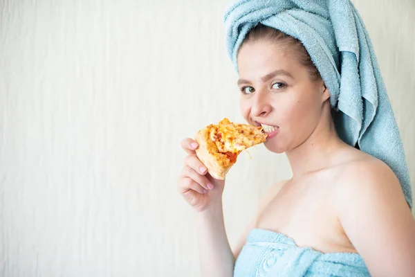 彼女の頭の上にタオルを持つかわいい女の子は、ベッドでピザを食べます。ベッドでファーストフードを食べている若い女性の肖像画。ボディポジティブ — ストック写真
