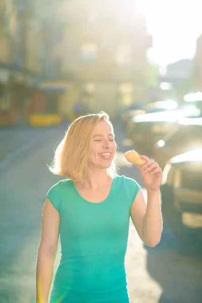 Portrét hezké dívky v zelených šatech chodí na dvoře a jí zmrzlinu. Krásná blondýnka se za krásného letního dne stravuje venku. Život je rekreační dovolená — Stock fotografie