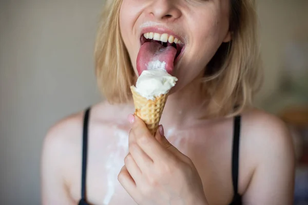 Sexy bionda lecca un cono cialda. Il gelato si sta sciogliendo, drenando eroticamente attraverso il corpo di una donna attraente. Bella ragazza in biancheria intima nera spalmata di gelato. Primo piano — Foto Stock