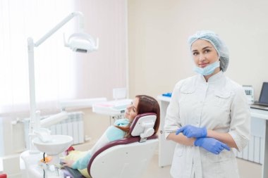 Genç güzel kadın dişçi geri ofiste hastaların arkasında duruyor. Kızıl saçlı kadın bir ortodontist ile bir sandalyede oturur ve gülümsüyor. Diş Hekimliği Hizmetleri. Arkadan görünüm