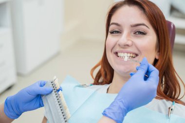 Dişçi sandalyesinde dişlerin rengini kontrol edin ve seçin. Dişçi güzel bir genç Kızıl saçlı kız tedavi sürecini yapar. Diş implantı seçimi. Close.
