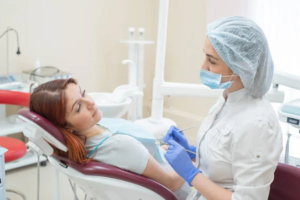 Joven dentista hermosa mujer ayuda a paciente con dolor de muelas. Mujer pelirroja se sienta en una silla en el médico en el examen. Servicios dentales . —  Fotos de Stock