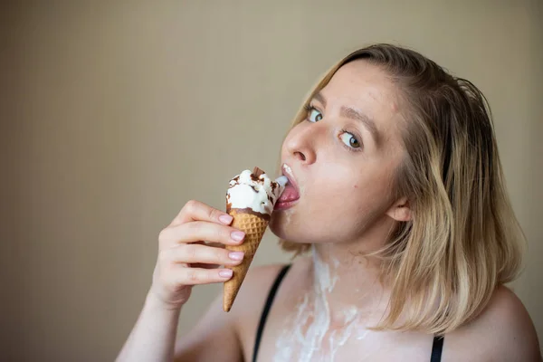 Sexy blonde licks a waffle cone. Ice cream is melting, erotically draining through the body of an attractive woman. Beautiful girl smeared with ice cream. — Stock Photo, Image