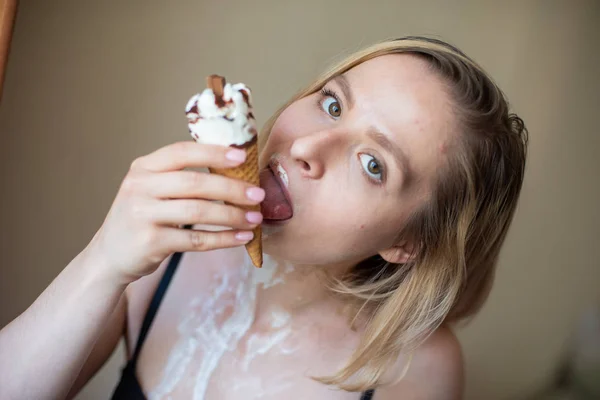 Sexy blonde licks a waffle cone. Ice cream is melting, erotically draining through the body of an attractive woman. Beautiful girl smeared with ice cream. — Stock Photo, Image