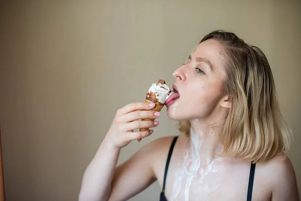 Sexy bionda lecca un cono cialda. Il gelato si sta sciogliendo, drenando eroticamente attraverso il corpo di una donna attraente. Bella ragazza spalmata di gelato. — Foto Stock