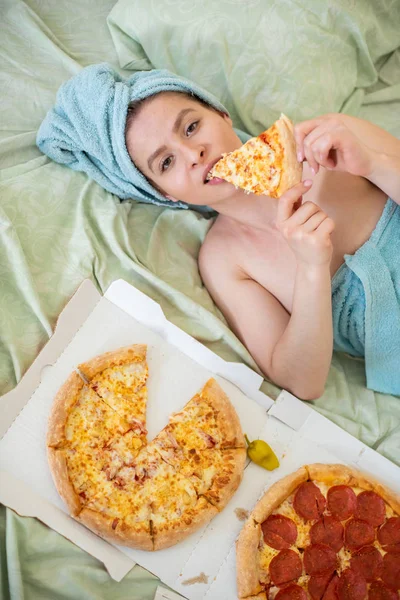 Jolie fille avec une serviette sur la tête mange de la pizza au lit. Jeune femme mangeant de la pizza au lit. La vie est un plaisir, corps positif. L'amour pour la cuisine italienne. Habitudes alimentaires, dépendance à la restauration rapide . — Photo