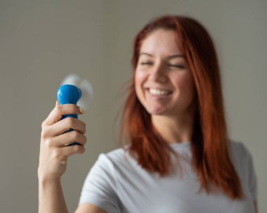 Elinde cep fanı olan kırmızı saçlı gülümseyen bir kadının portresi. Kablosuz bir elektrikli cihazdan bir rüzgar darbe ısı serinletici bir kızın tam yüzü. Klimanın serin hava akışı