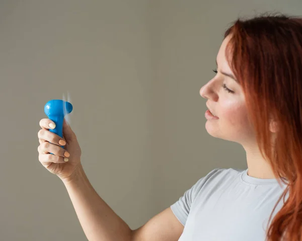 Ritratto di una donna dai capelli rossi con un ventilatore tascabile in mano. Profilo di una ragazza rinfrescata nel calore da un vento soffiato da un dispositivo elettrico wireless. Godetevi il flusso d'aria fresca dal condizionatore . — Foto Stock