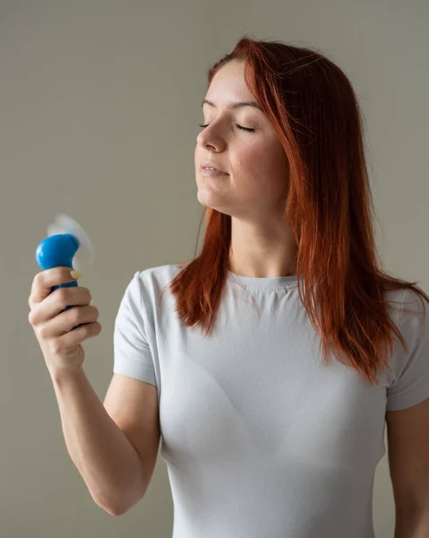 Ritratto di una donna dai capelli rossi con un ventilatore tascabile in mano. Profilo di una ragazza rinfrescata nel calore da un vento soffiato da un dispositivo elettrico wireless. Godetevi il flusso d'aria fresca dal condizionatore . — Foto Stock