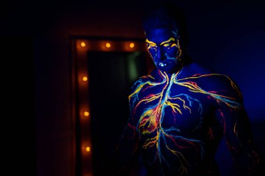 Ultraviyole desenli vücut sanatı bir erkeğin vücudunda dolaşım sistemi. Kaslı bir atletin gövdesinde, damarlar ve arterler floresan boyalarla çizilir. Beden geliştirici elinde lambalarla aynanın karşısında duruyor..