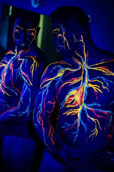 Modelli UV body art del sistema circolatorio su un corpo umano. Sul petto di un atleta muscolare, vene e arterie sono disegnate con coloranti fluorescenti. Bodybuilder è in piedi allo specchio . — Foto Stock