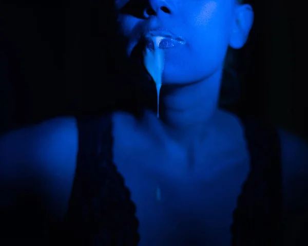 A thick white liquid flows down the lips of a young European girl. Dripping down. Ultraviolet, blue light. Close-up portrait. Spit out. — Stock Photo, Image