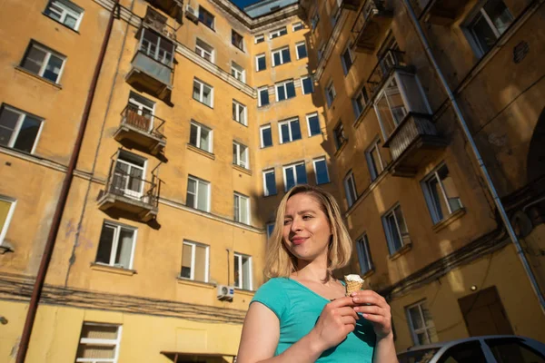 Linda chica en un vestido verde está comiendo helado en el patio de una casa vieja. Una hermosa mujer rubia está comiendo postre afuera en un hermoso día de verano. La vida es un placer, un cuerpo positivo. Hábitos alimentarios —  Fotos de Stock