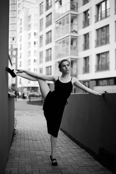 Ballerina in tutu makes an elegant pose. Beautiful young woman in black dress and pointe dancing over city background. Portrait of a gorgeous ballerina performing a dance outdoors. Black and white — Stock Photo, Image