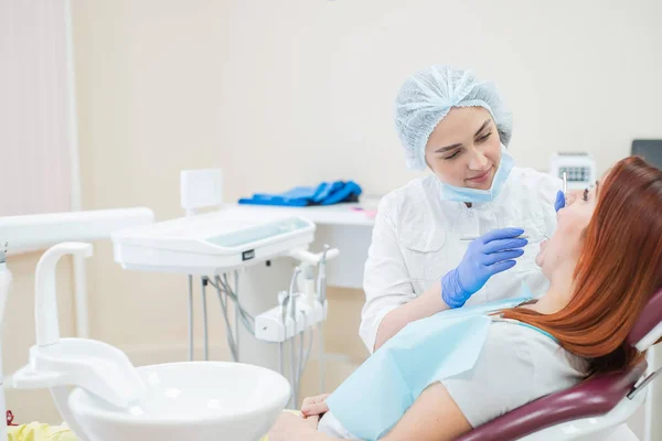 Uma dentista a verificar a cárie da paciente. Mulher ruiva examinada por um médico. A menina vai fazer a saúde dos dentes . — Fotografia de Stock