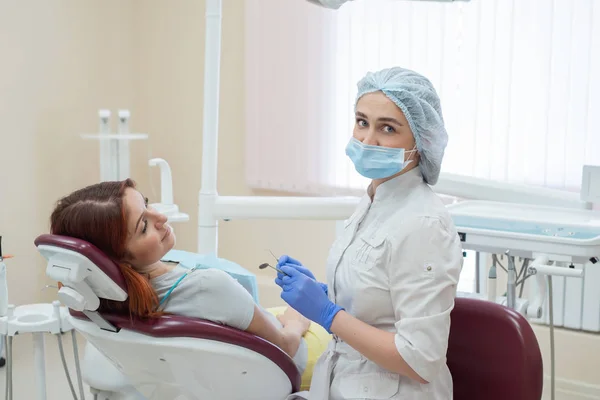 Молода красива жінка-стоматолог допомагає пацієнту з зубним болем. Червоноволоса жінка сидить на стільці у лікаря на огляді. Стоматологічні послуги . — стокове фото