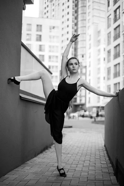 Ballerina in tutu makes an elegant pose. Beautiful young woman in black dress and pointe dancing over city background. Portrait of a gorgeous ballerina performing a dance outdoors. Black and white — Stock Photo, Image