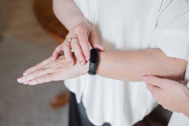 Beyaz bluz giymiş yaşlı bir kadın fitness bileziği takıyor. Yaşlı bir kadının elinde akıllı saat. Fitness Tracker kullanarak Emekli.