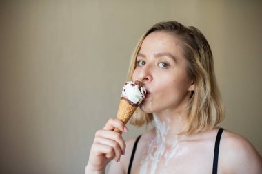 Seksi sarışın waffle külahını yalıyor. Dondurma eriyor, erotik olarak çekici bir kadının vücudunu emiyor. Dondurma sürülmüş güzel kız.