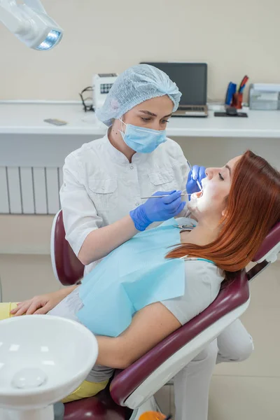 Mujer dentista revisando a su paciente en busca de caries. Mujer pelirroja examinada por un médico. La chica hará la salud de los dientes . —  Fotos de Stock