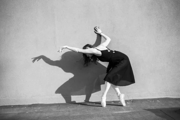 Ballerina in Tutu poseren staande in de buurt van de muur. Mooie jonge vrouw in zwarte jurk en Pointe dansen over stad achtergrond. Prachtige ballerina die een dans buitenshuis uitvoert. Zwart-wit — Stockfoto