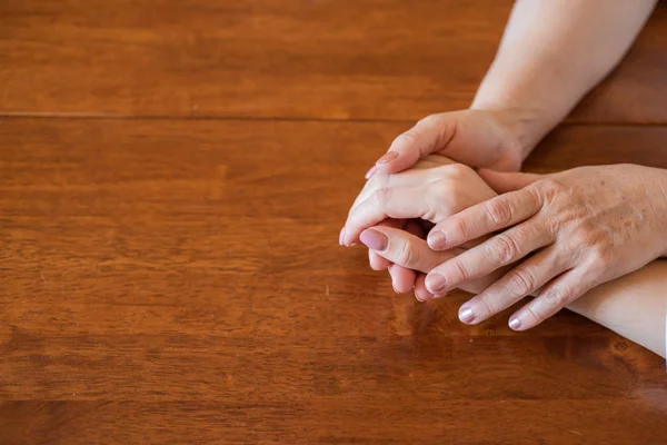 Elderly mother and her daughter holding hands while sitting at the table.Close up on women of different generations holding hands. Close Up Shot Of Mother And Daughter\'s Hands Holding