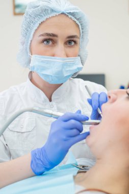 Beyaz üniformalı çekici bir bayan doktor kızıl saçlı bir hastayı muayene ediyor. Dişçi dişleri matkapla tedavi ediyor. Yakın plan.