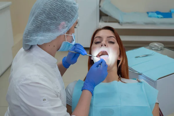 Mujer dentista revisando a su paciente en busca de caries. Mujer pelirroja examinada por un médico. La chica hará la salud de los dientes . — Foto de Stock