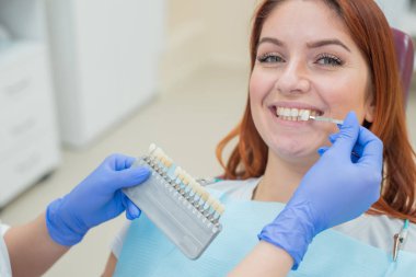 Dişçi sandalyesinde dişlerin rengini kontrol edin ve seçin. Dişçi güzel bir genç Kızıl saçlı kız tedavi sürecini yapar. Diş implantı seçimi. Close.