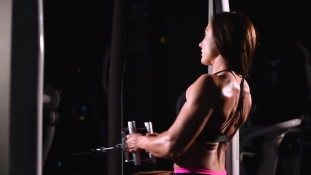 Una chica fuerte, musculosa y atlética, en pantalones cortos, entrena los músculos de la espalda en un simulador horizontal en un gimnasio oscuro . — Vídeos de Stock