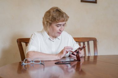 Beyaz bluzla güzel yaşlı kadın masada oturuyor ve telefona mesajlar yazıyor. Emekli kadın puan aldı ve akıllı telefonmesajı okur