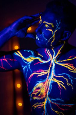 Ultraviyole desenli vücut sanatı bir erkeğin vücudunda dolaşım sistemi. Kaslı bir atletin gövdesinde, damarlar ve arterler floresan boyalarla çizilir. Beden geliştirici elinde lambalarla aynanın karşısında duruyor..