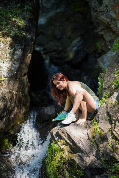 Red-haired woman in shorts doing yoga at the waterfall. The girl is standing in the pose of a firefly, titibhasana — Stock Photo, Image