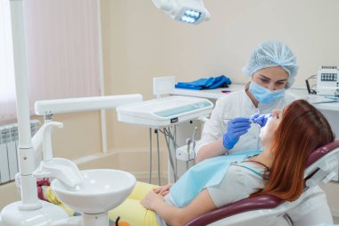 Kadın diş hekimi hastasını çürük için kontrol ediyor. Kızıl saçlı kadın bir doktor tarafından muayene edildi. Kız dişlerin sağlığını yapacak..