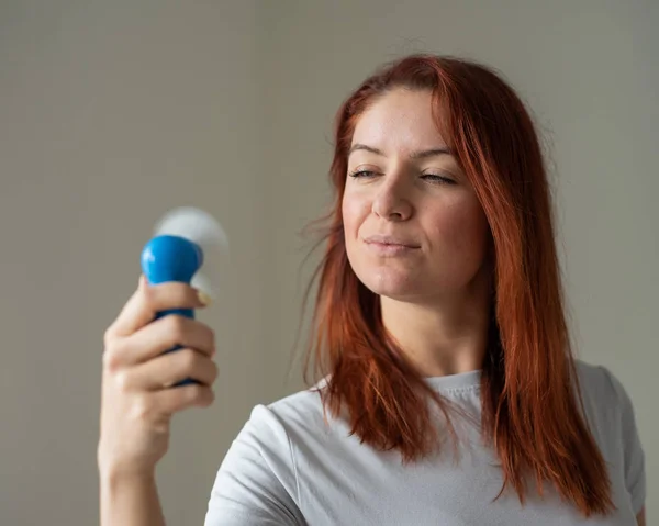 Retrato de una mujer pelirroja con un abanico de bolsillo en las manos. Una chica refrescante en el calor del viento que sopla lejos de un dispositivo eléctrico inalámbrico. Disfrute del flujo de aire fresco del aire acondicionado . — Foto de Stock