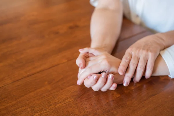 Elderly mother and her daughter holding hands while sitting at the table.Close up on women of different generations holding hands. Close Up Shot Of Mother And Daughters Hands Holding — Stock Photo, Image