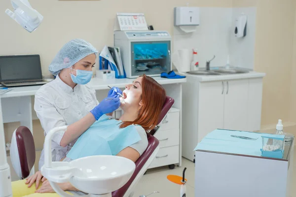 Mujer dentista revisando a su paciente en busca de caries. Mujer pelirroja examinada por un médico. La chica hará la salud de los dientes . —  Fotos de Stock