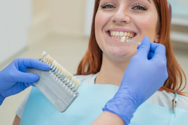 Controllare e selezionare il colore dei denti sulla sedia del dentista. Il dentista fa il processo di trattamento di una bella giovane ragazza dai capelli rossi. Selezione di un impianto dentale. Primo piano . — Foto Stock