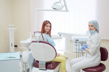 Bir kadın diş hekimi ve diş tedavisi sonrası bir ofiste kızıl saçlı hasta mutlu yüzleri ile kameraya bakıyor. Mutlu kadın, gösterileri aldıktan sonra doktoruyla birlikte. Diş hizmetleri. 