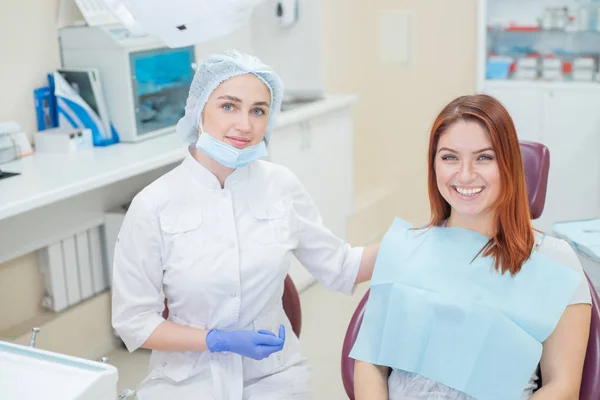 Joven dentista hermosa mujer ayuda a paciente con dolor de muelas. Mujer pelirroja se sienta en una silla en el médico en el examen. Servicios dentales . —  Fotos de Stock