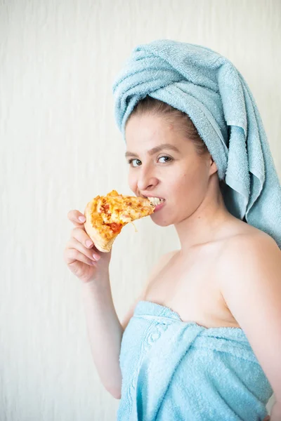 Schattig meisje met een handdoek op haar hoofd eet pizza in bed. Portret van een jonge vrouw eten Fast Food in bed. Bodypositive — Stockfoto